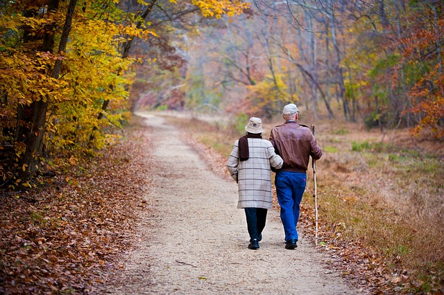 Couple se promenant dans une forêt en automne avec les feuilles de couleur orangées et marron. 